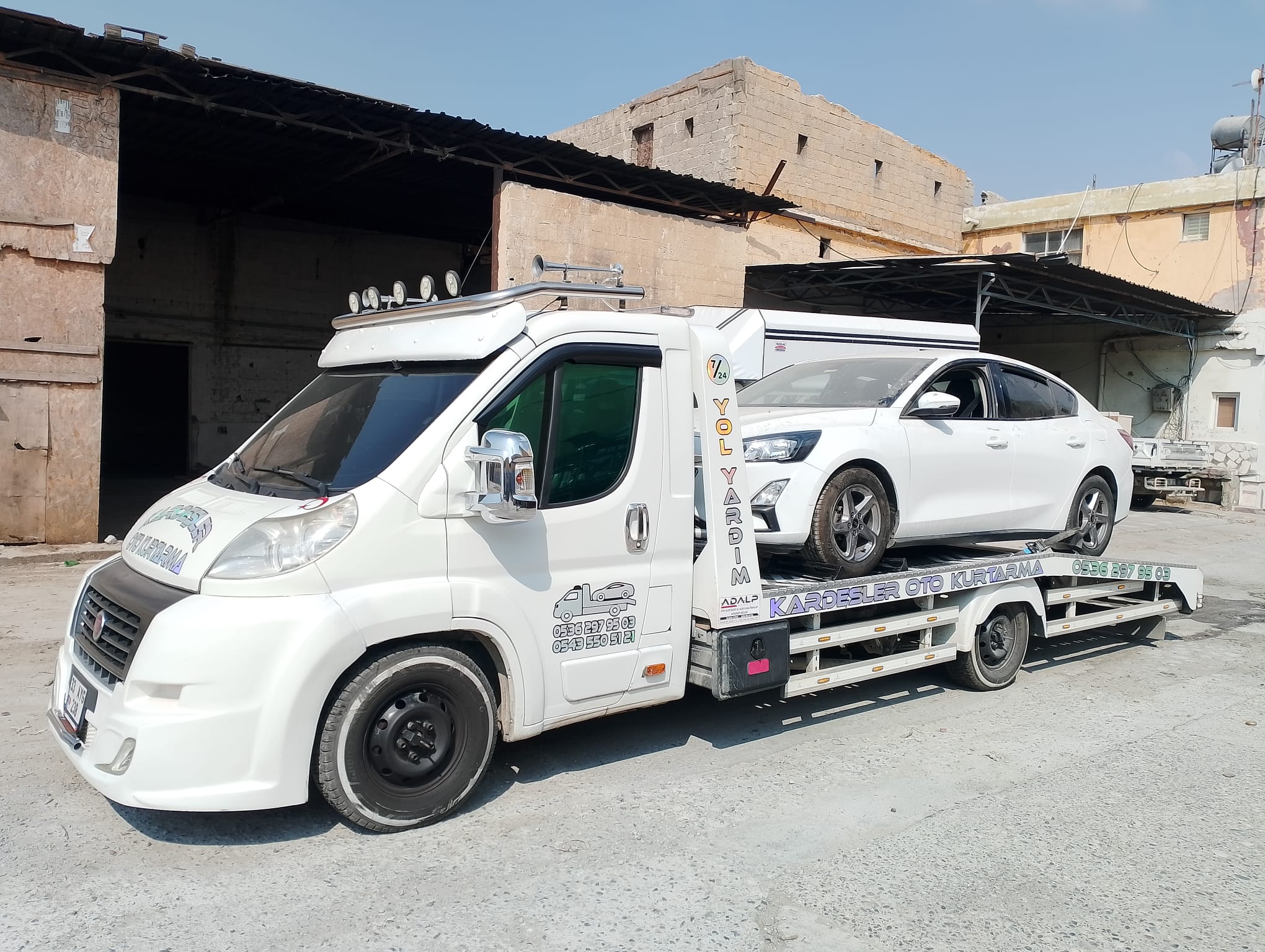 Garaj önünde çekiciye yüklenmiş beyaz otomobil — Kardeşler Oto Kurtarma